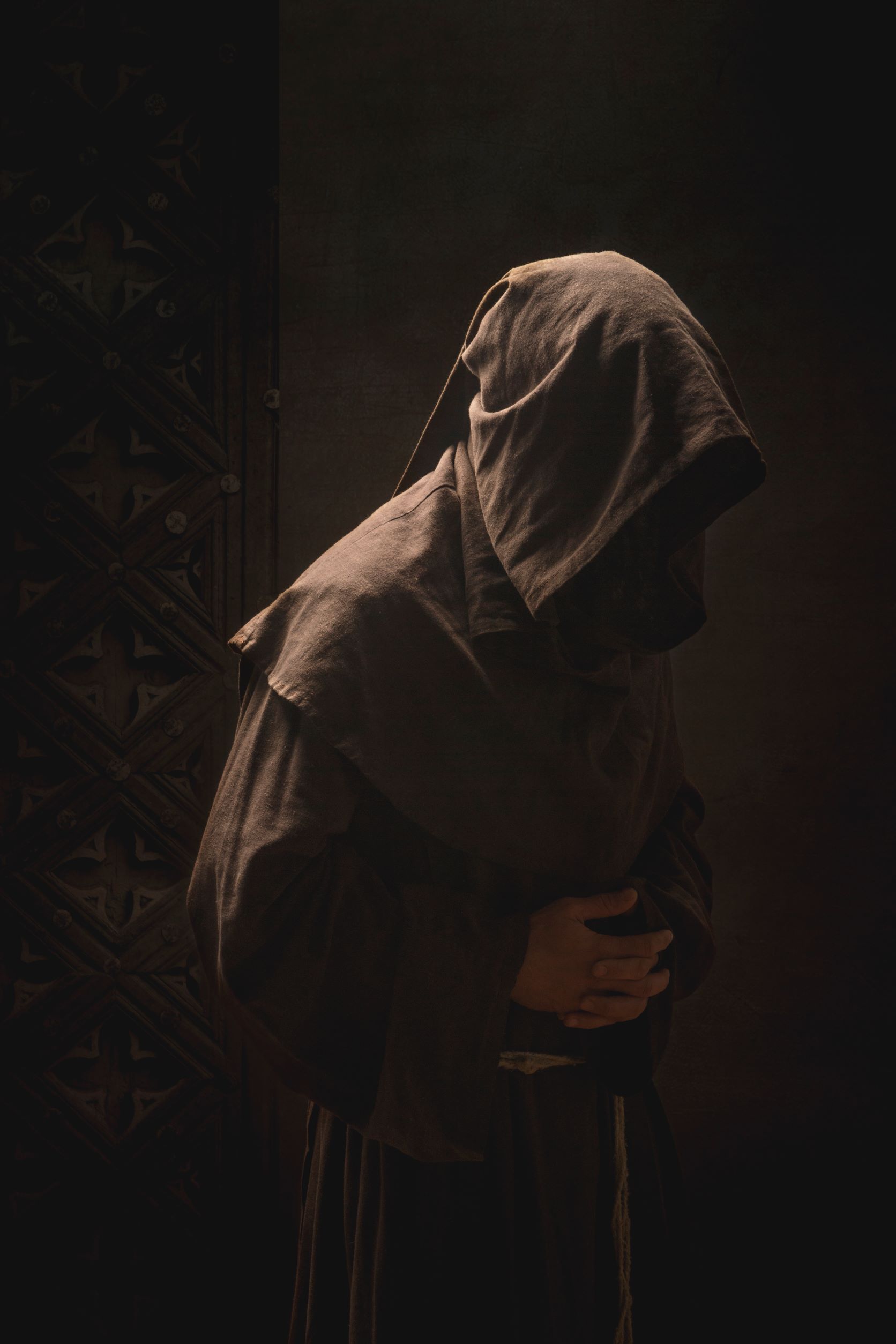 Fotografia przedstawia postać zakonnika w kapturze na ciemnym tle.