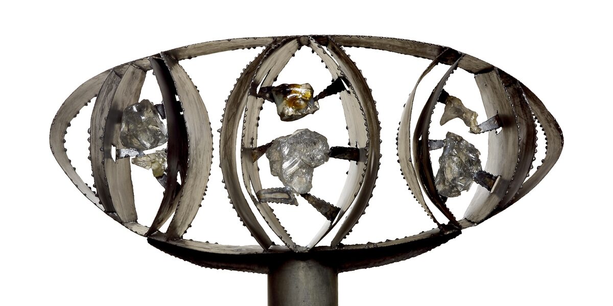 Rzeźba z metalu i kamieni w formie elipsy osadzonej w krótkim słupie