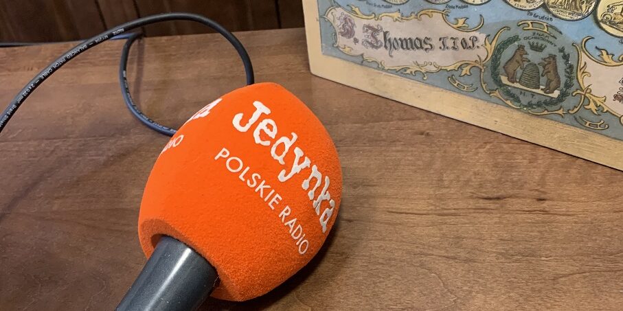 Zdjęcie przedstawia pomarańczowy mikrofon Programu Pierwszego Polskiego Radia, który został położony na ladzie sklepowej, na wystawie. Obok została ustawiona drewniana skrzynka do pierników.