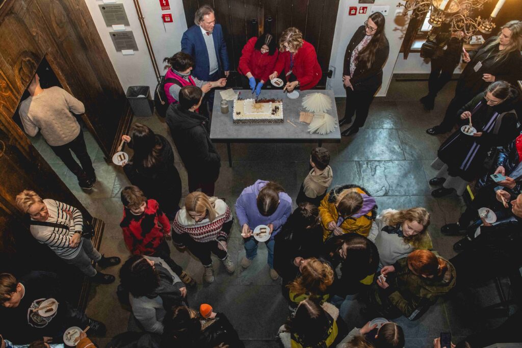 Zdjęcie wykonane z góry przedstawia osoby jedzące tort przy prostokątnym stole.